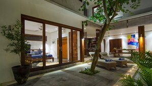 Un área exterior moderna con zona de estar, un gran ventanal corredero que da a un dormitorio y una zona de comedor con mesa y sillas.