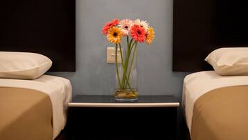 Habitación de hotel con dos camas, una mesita de noche con un florero y un interruptor de luz en la pared.