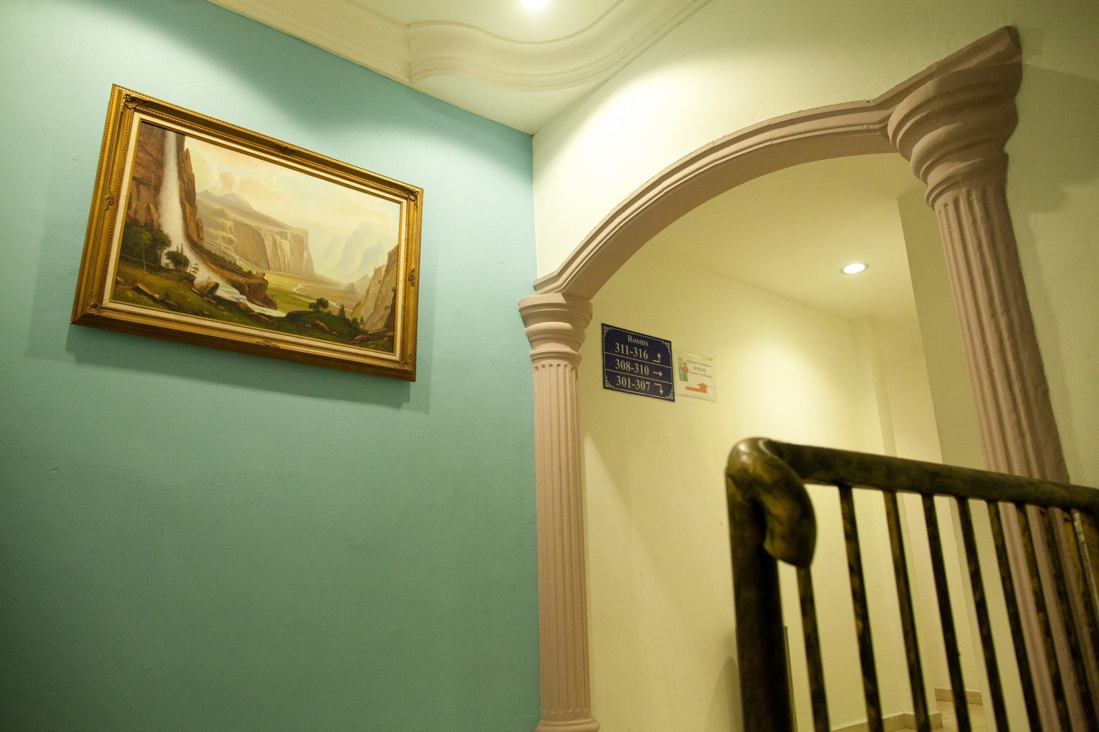 A staircase with a classical design, a framed painting on the wall, and directional signs for rooms.
