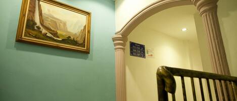 A staircase with a classical design, a framed painting on the wall, and directional signs for rooms.