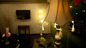 A lamp with a textured shade and tassels, a television mounted on the wall, and a chair in a dimly lit room. - Hotel Ria (Johor Bahru)