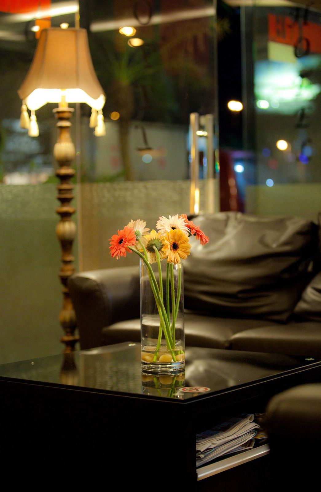 Un jarrón de vidrio con flores sobre una mesa en una habitación con una lámpara y un sofá.