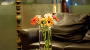 Un jarrón de vidrio con flores sobre una mesa en una habitación con una lámpara y un sofá.