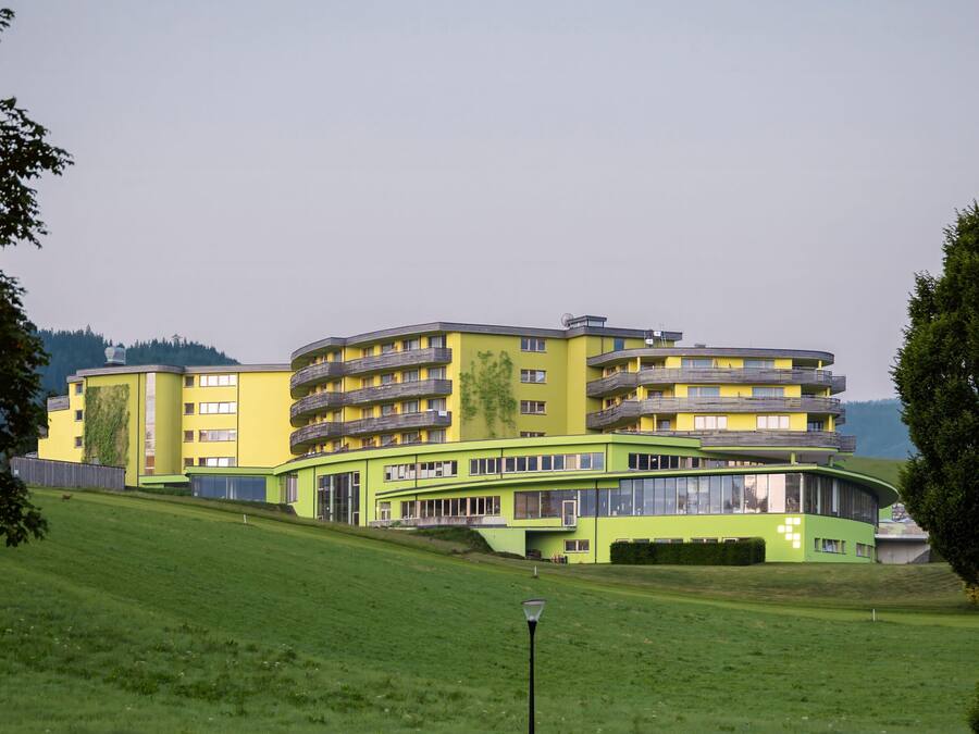 Een modern meerlaags gebouw met balkons, omgeven door een verzorgd gazon en een lantaarnpaal.