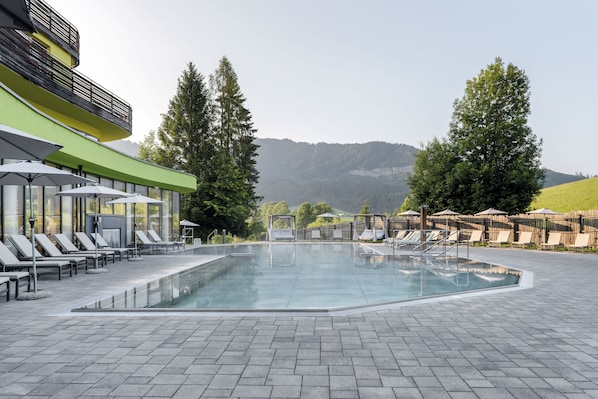 A swimming pool with lounge chairs and umbrellas, surrounded by trees and a view of hills.
