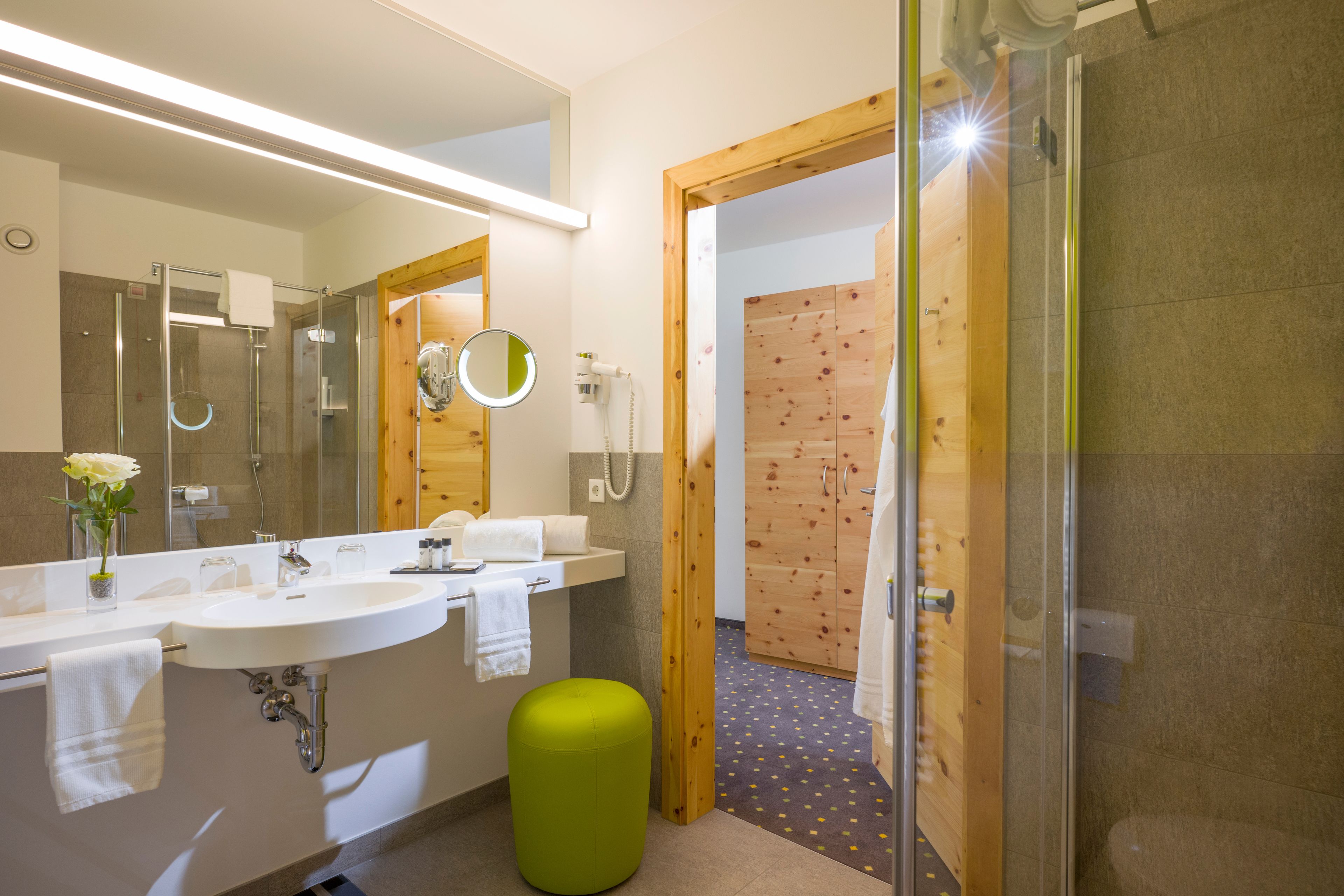 A modern bathroom with a large mirror, two sinks, a shower, and a toilet.
