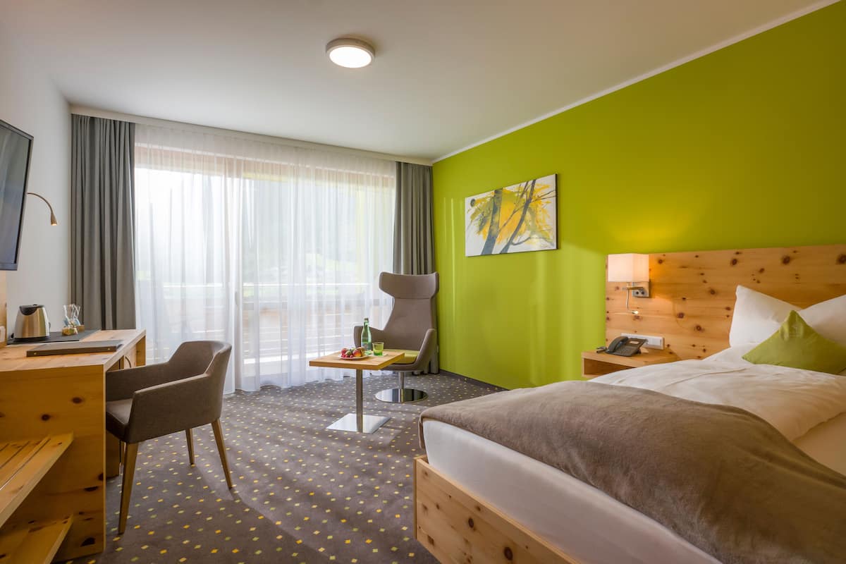 A hotel room with a bed, a desk, a chair, a small table, and a window with curtains.