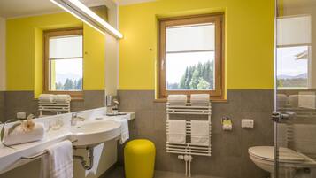 Un baño con una pared amarilla, un ventanal grande, un lavamanos, un inodoro y un taburete amarillo.