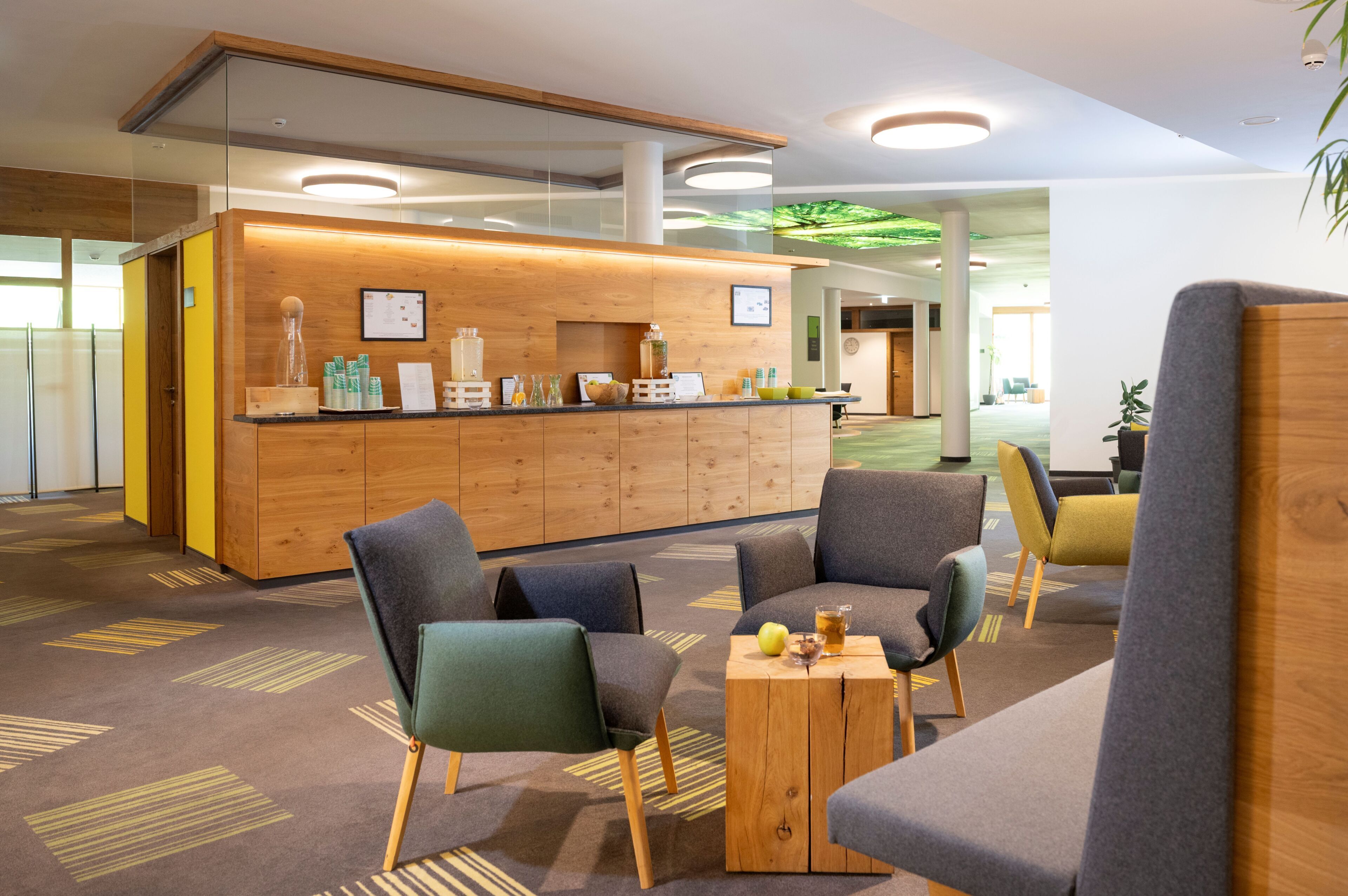 A modern reception area with a wooden counter, seating with cushions, and a patterned carpet.