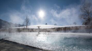 A hot spring pool with steam rising, surrounded by snow-covered hills and a clear sky.