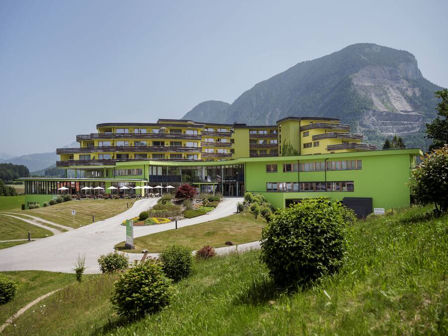Een hotel met meerdere verdiepingen, een groene gevel, een terras en een berg op de achtergrond.