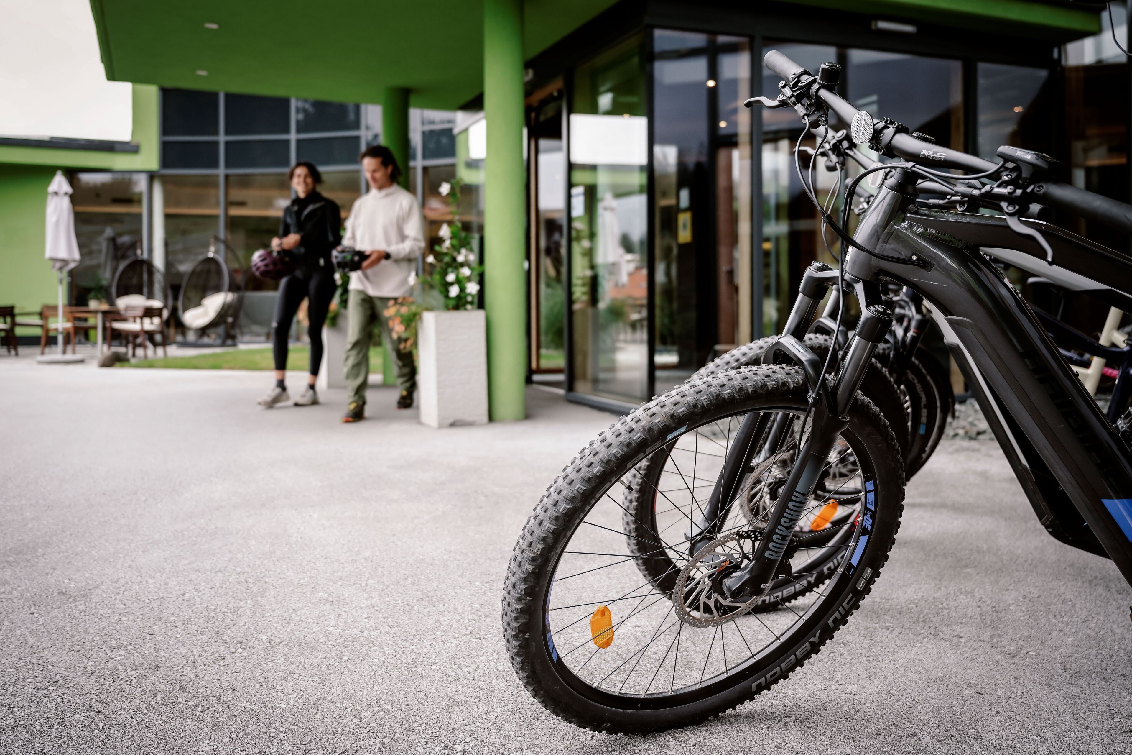 A bicycle parked in front of a building with a green exterior and large windows.