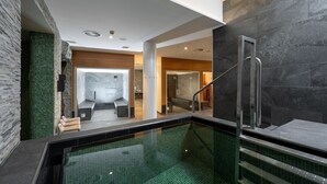 A modern indoor swimming pool with a glass wall, a staircase, and a view into a spa area. - DAS SIEBEN ****s - Adults Only (Bad Haering)
