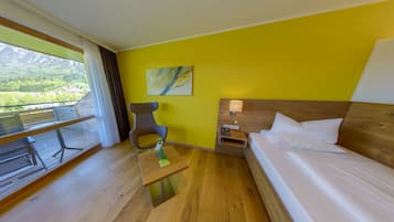 A hotel room with a bed, a desk, a chair, a table, a phone, and a painting on the wall.