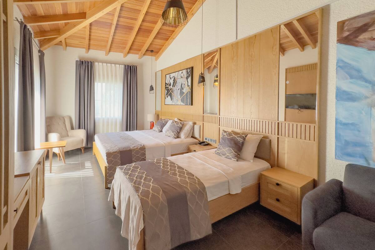 A hotel room with two beds, a sofa, a desk, and a large window with curtains.