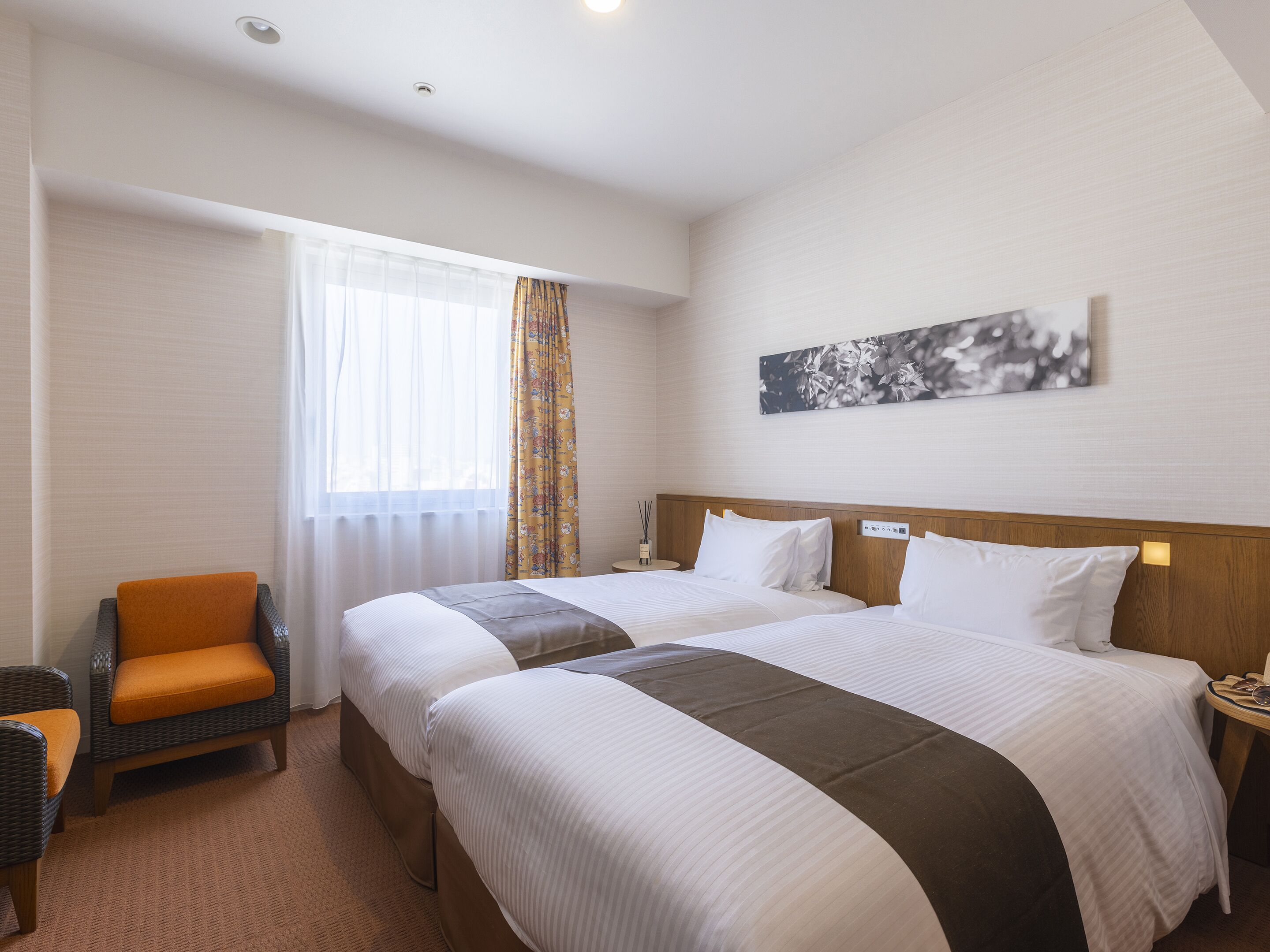 A hotel room with two beds, a chair, a nightstand, and a window with curtains.