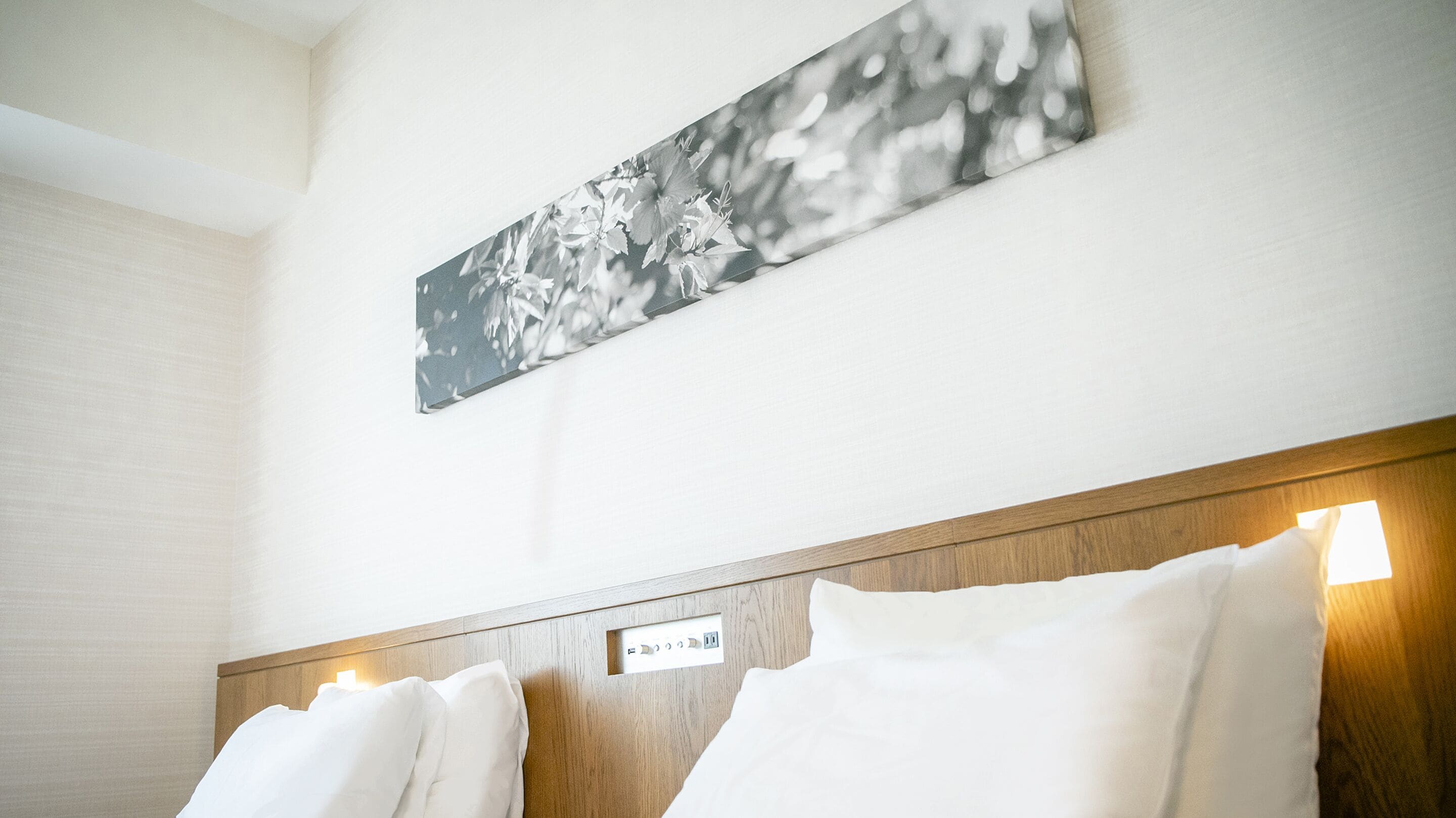 A hotel room with a wooden headboard, two white pillows, and a wall-mounted artwork.