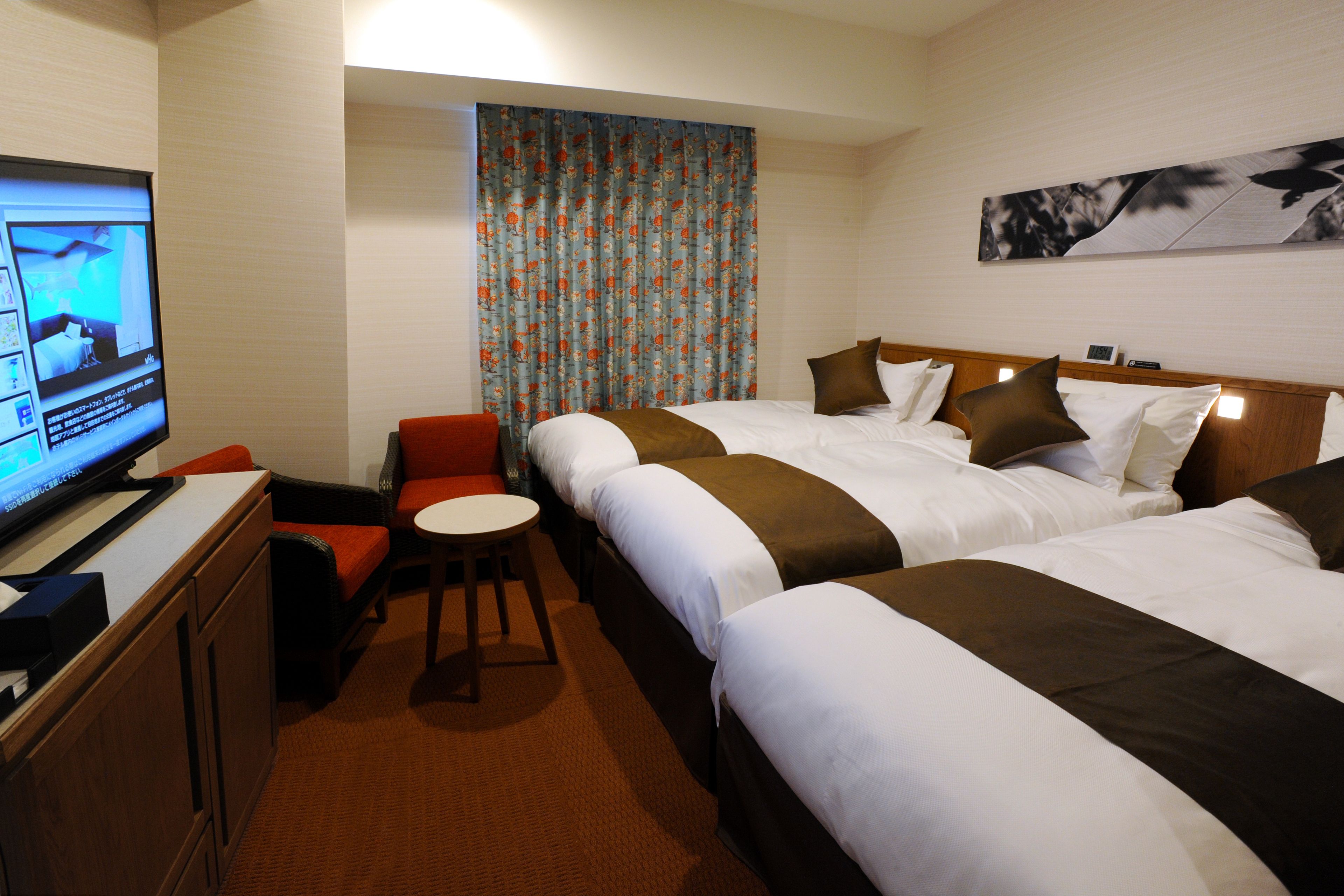 A hotel room with two beds, a TV, a small table, and a red chair.