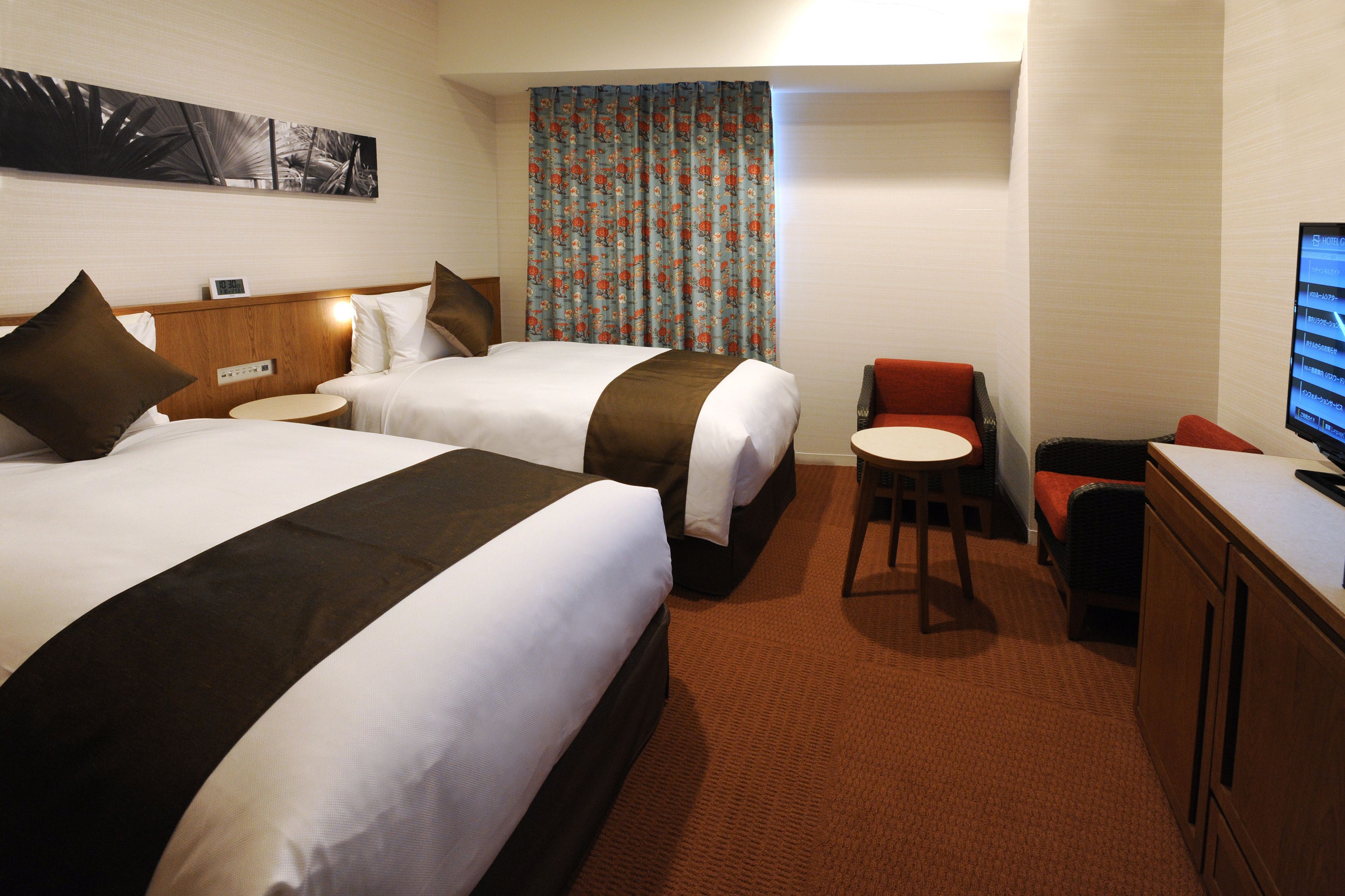 Une chambre d’hôtel avec deux lits, une petite table ronde, un téléviseur et une chaise rouge.