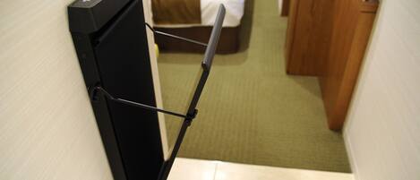 A hotel room with a bed, a desk, and a black luggage cart.