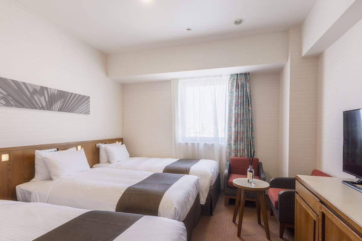 Hotellihuone, jossa on kaksi sänkyä, pieni pöytä, televisio ja ikkuna, jossa on verhot.