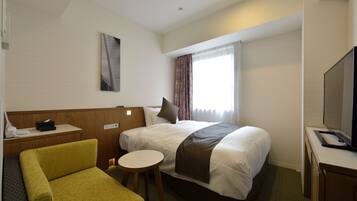 A hotel room with a bed, a small desk, a chair, a television, and a window with curtains.