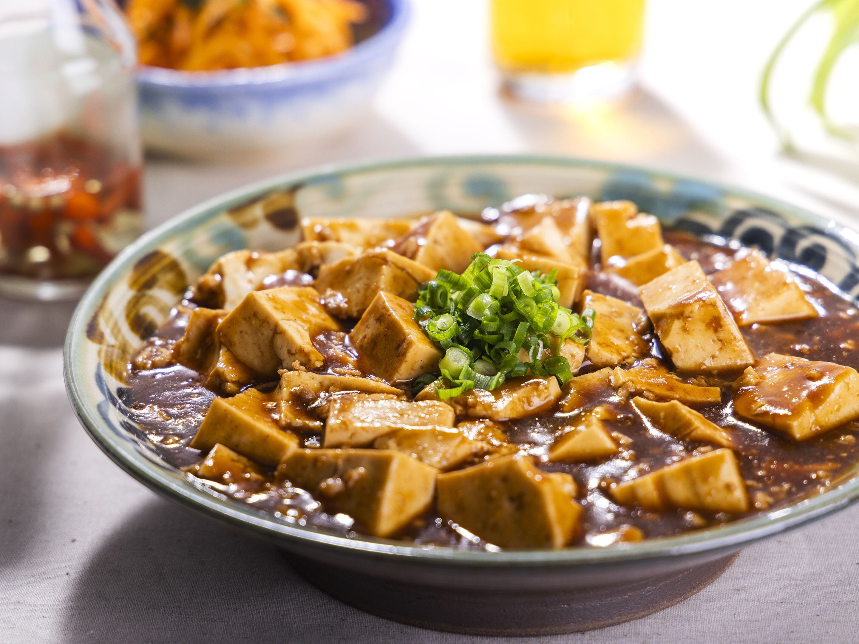 A bowl of tofu with a dark sauce and green onions, served on a plate.