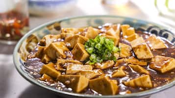 A bowl of tofu with a dark sauce and green onions, served on a plate.