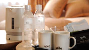 Habitación de hotel con una cama, una mesita de noche con una tetera, dos botellas de agua, dos tazas blancas con la inscripción