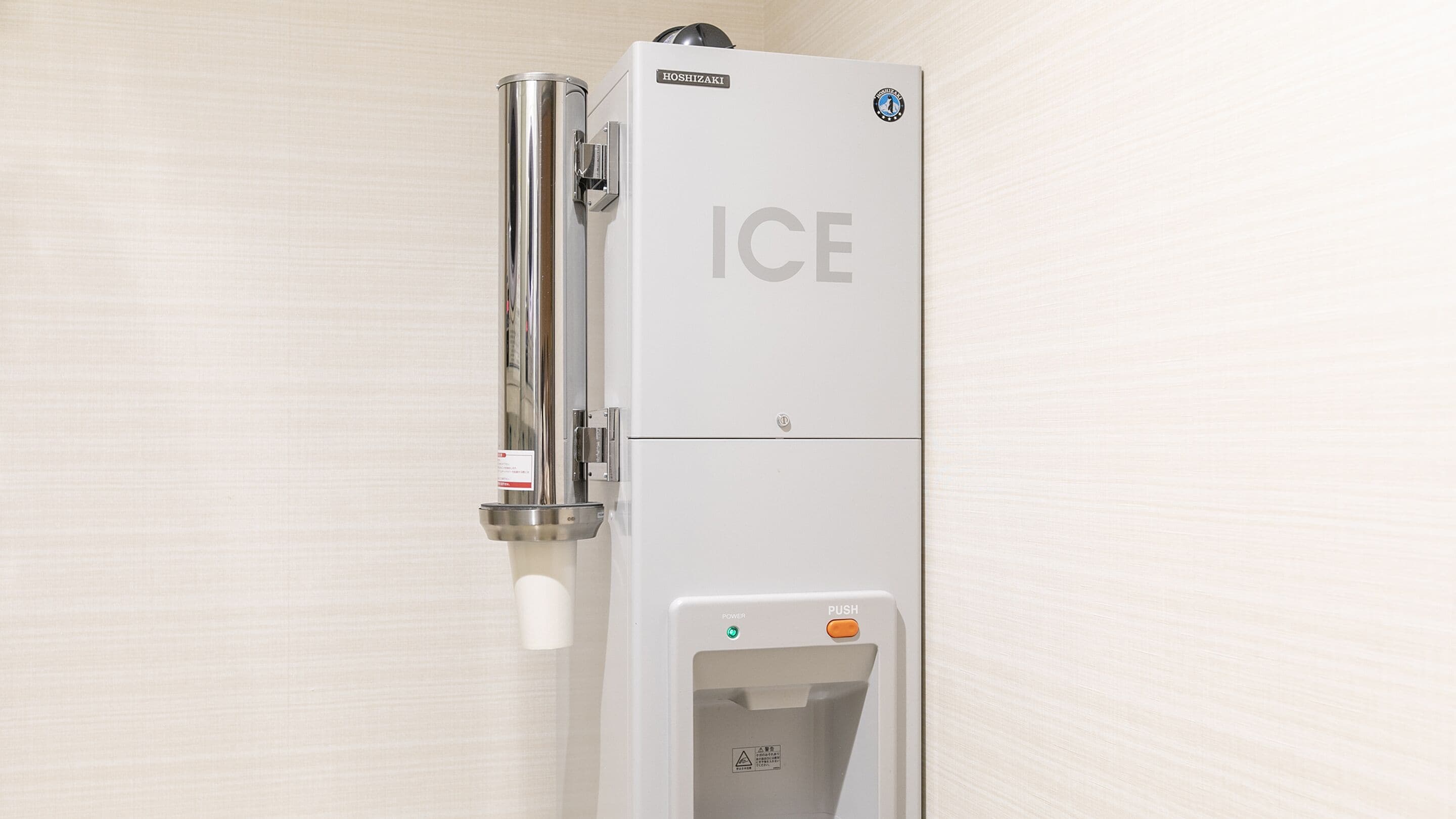 A white ice dispenser with a pull-down spout and a push button, labeled "ICE".