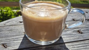 A glass mug of coffee on a wooden table with a scenic view of mountains and greenery in the background. - Yggdrasil Farmhotel Retreat, Spa & Yoga (Tromsø)