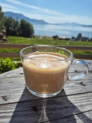 A glass mug of coffee on a wooden table with a scenic view of mountains and greenery in the background. - Yggdrasil Farmhotel Retreat, Spa & Yoga (Tromsø)