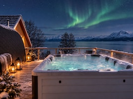 A hot tub with a view of snow-capped mountains and the Northern Lights.