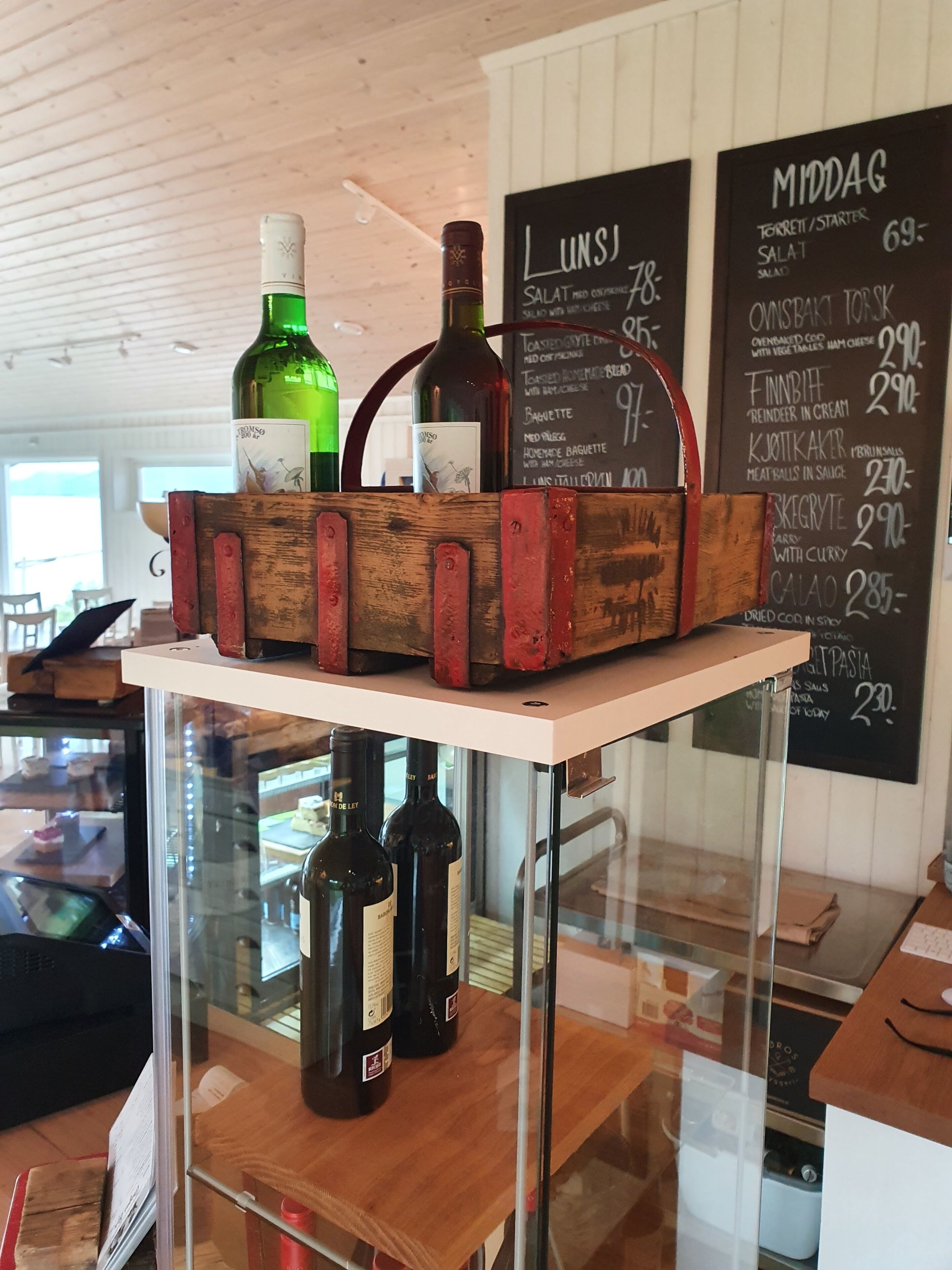 A wooden crate with bottles on a shelf, a menu board with food items, and a glass display case with bottles.