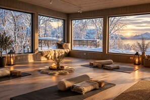 A spacious room with large windows, a wooden floor, a seating area with a bench, and a small tree.