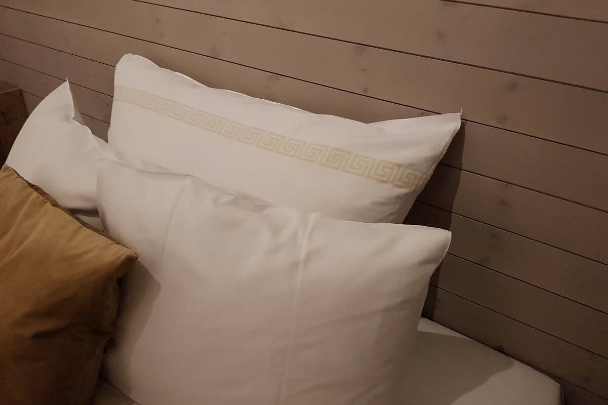 Ein Bett mit Kissen, einem Holz-Kopfende und einem braunen Kopfkissen.