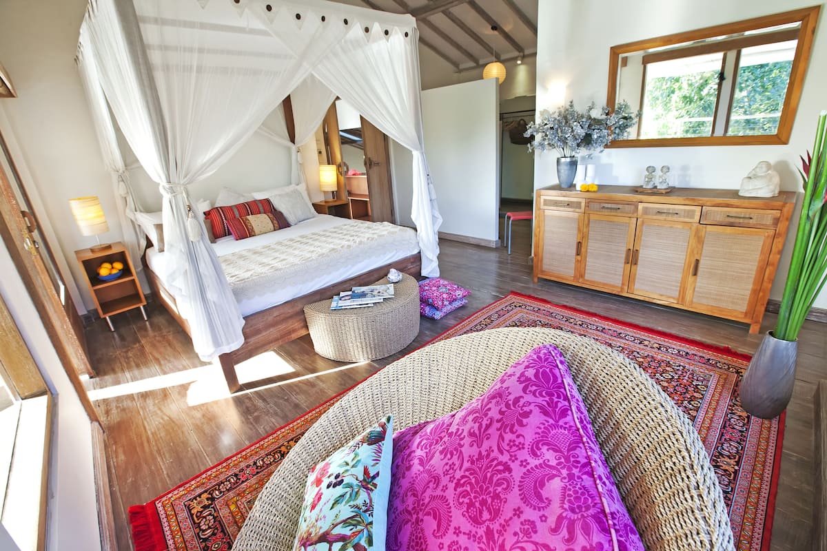 Un dormitorio con una cama con dosel, una cama tipo diván, un armario de madera y un ventanal grande.