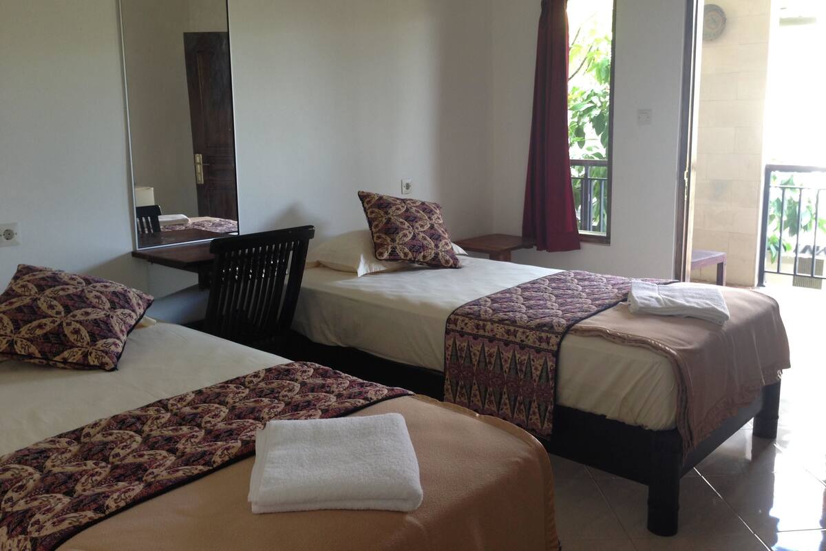 A hotel room with two beds, a mirror, a window with curtains, and a view of the outside.