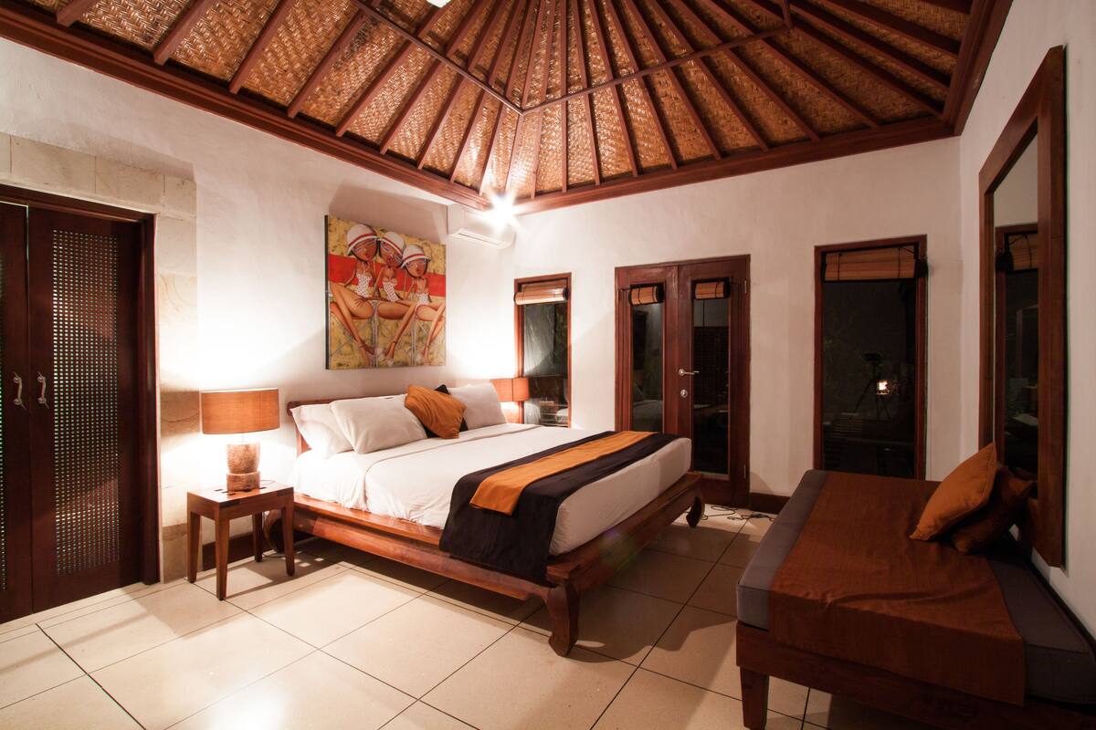A bedroom with a large bed, a wooden bench, a nightstand, and a ceiling fan.