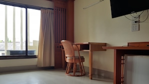 A room with a wooden desk, a wicker chair, a television, and a window with curtains. - PoonSook Resident Hotel (Phitsanulok)