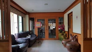 A reception area with a brown leather sofa, a tripod, and a pair of decorative ceramic shoes. - PoonSook Resident Hotel (Phitsanulok)