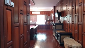 A hallway with wooden paneling, a wicker bench, and a television on the wall. - PoonSook Resident Hotel (Phitsanulok)