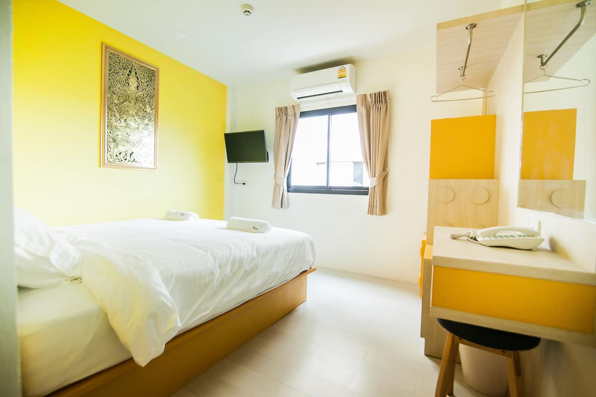Una habitación de hotel con cama, mesita de noche, espejo, ventana con cortinas, aire acondicionado y televisor montado en la pared.