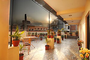 A rooftop terrace with a table and chairs, surrounded by potted plants and flowers.