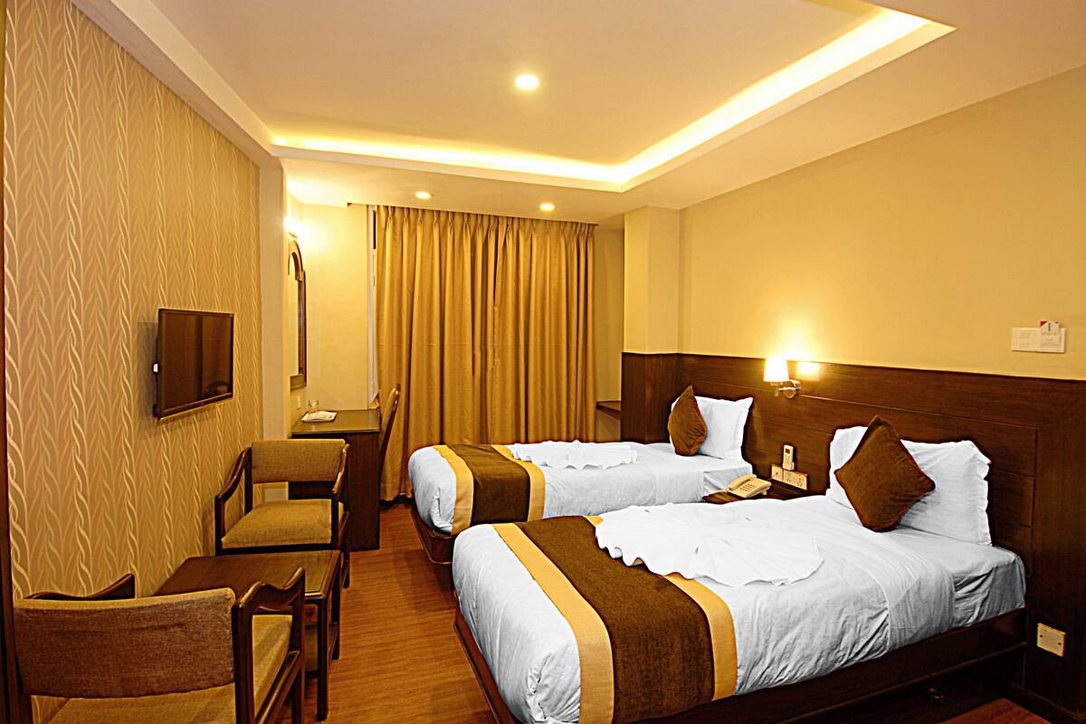 A hotel room with two beds, a desk, a chair, and a television.