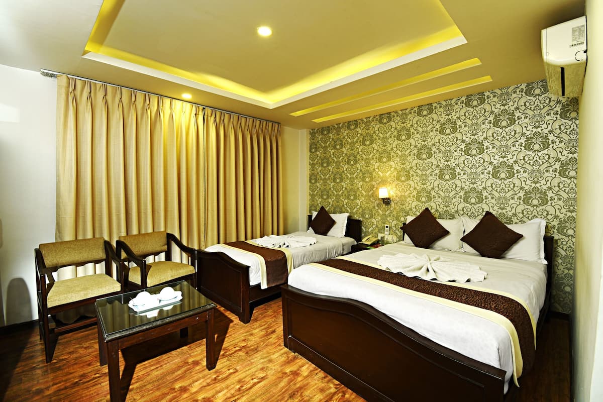 A hotel room with two beds, a sitting area with a table, and a patterned wallpaper.