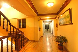 A hallway with wooden flooring, a staircase with wooden balusters, and a potted plant.