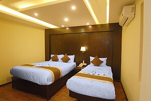 Habitación de hotel con dos camas, cabecero de madera, lámparas de noche y un equipo de aire acondicionado.