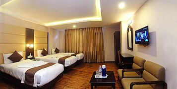 Habitación de hotel con dos camas, televisor, mesita de centro y sofá.