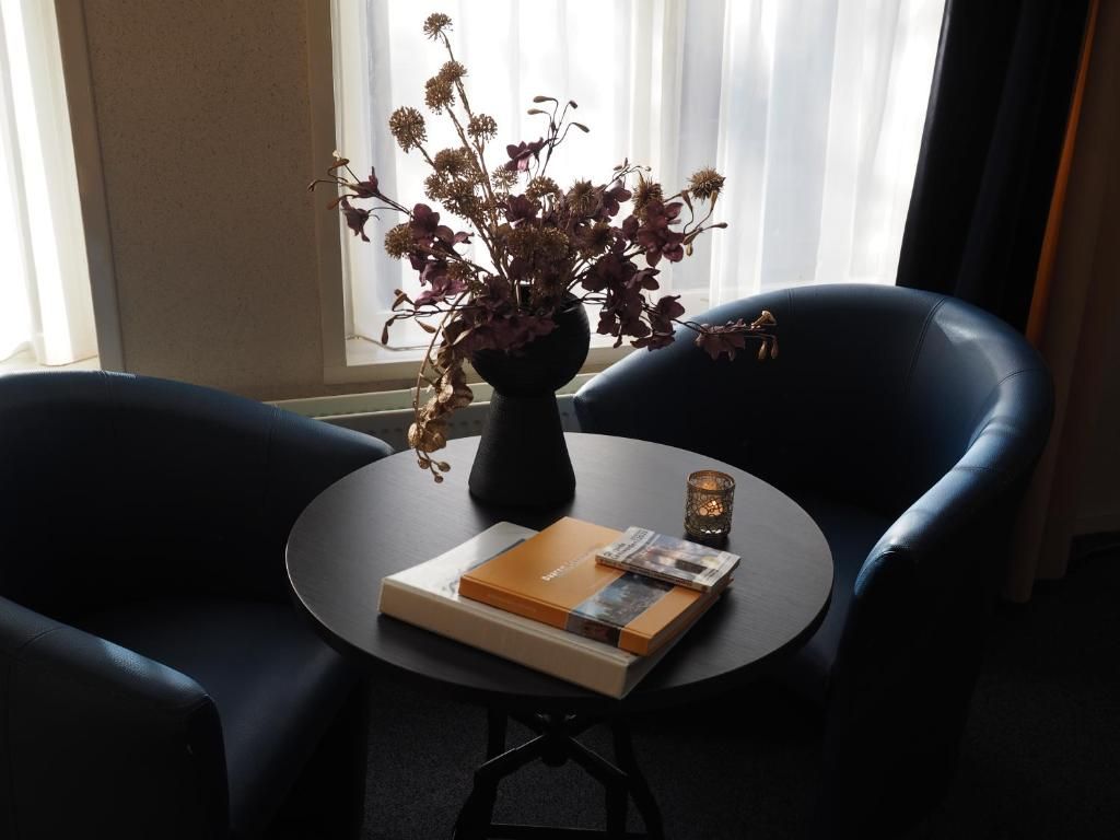 A room with a round table, two chairs, a vase with dried flowers, and a candle.